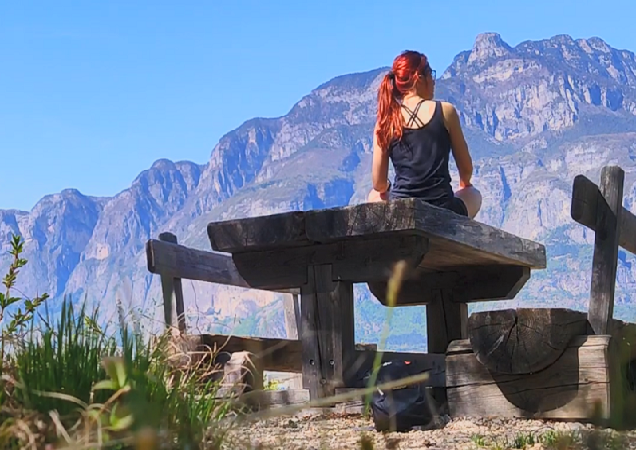 Barbara, red-haired girl, admiring the view of the mountains in Trentino while seated at a picnic table.